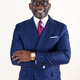 A man in spectacles, a blue pinstriped suit jacket, a white shirt, and a golden watch.